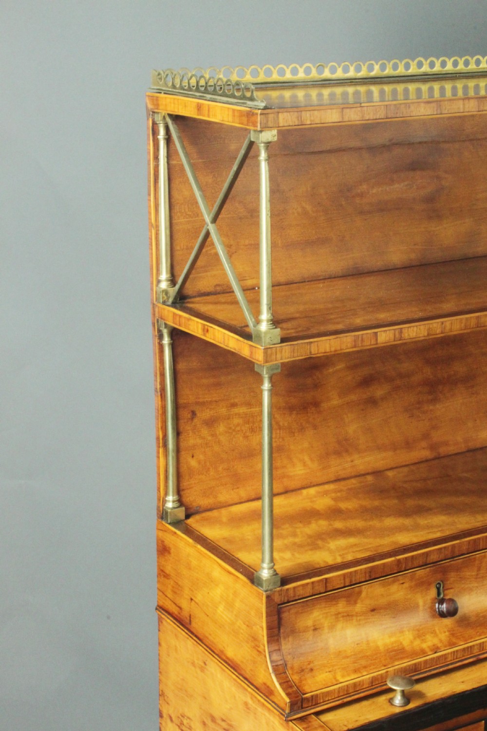 An antique satinwood cylinder bureau desk featuring an open two-tier bookshelf gallery at the top, a green leather writing surface inside, and tapered square legs with a low shelf. View III