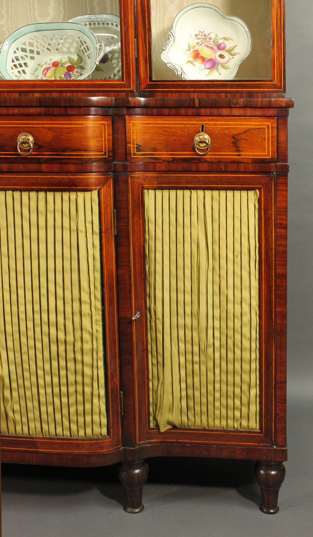 A Regency rosewood breakfront bookcase featuring four glazed upper doors and four lower doors lined with pleated fabric. View VII