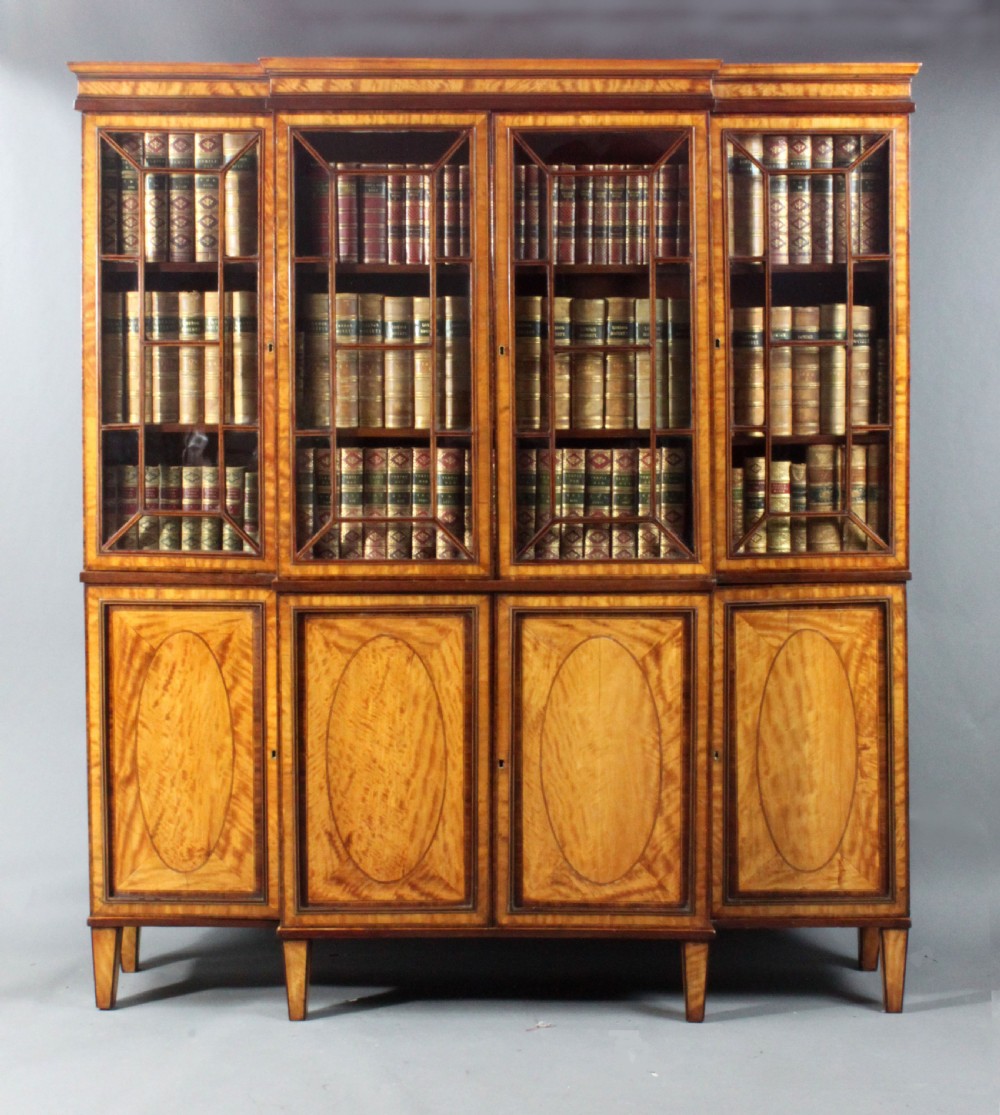 A four-door Georgian breakfront bookcase crafted from golden satinwood featuring geometric astragal glazing bars above four oval inlaid cupboard doors.