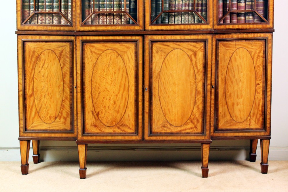 A four-door Georgian breakfront bookcase crafted from golden satinwood featuring geometric astragal glazing bars above four oval inlaid cupboard doors. View II