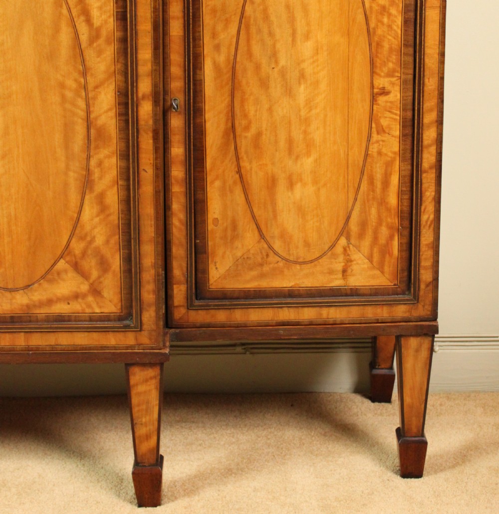 A four-door Georgian breakfront bookcase crafted from golden satinwood featuring geometric astragal glazing bars above four oval inlaid cupboard doors. View III