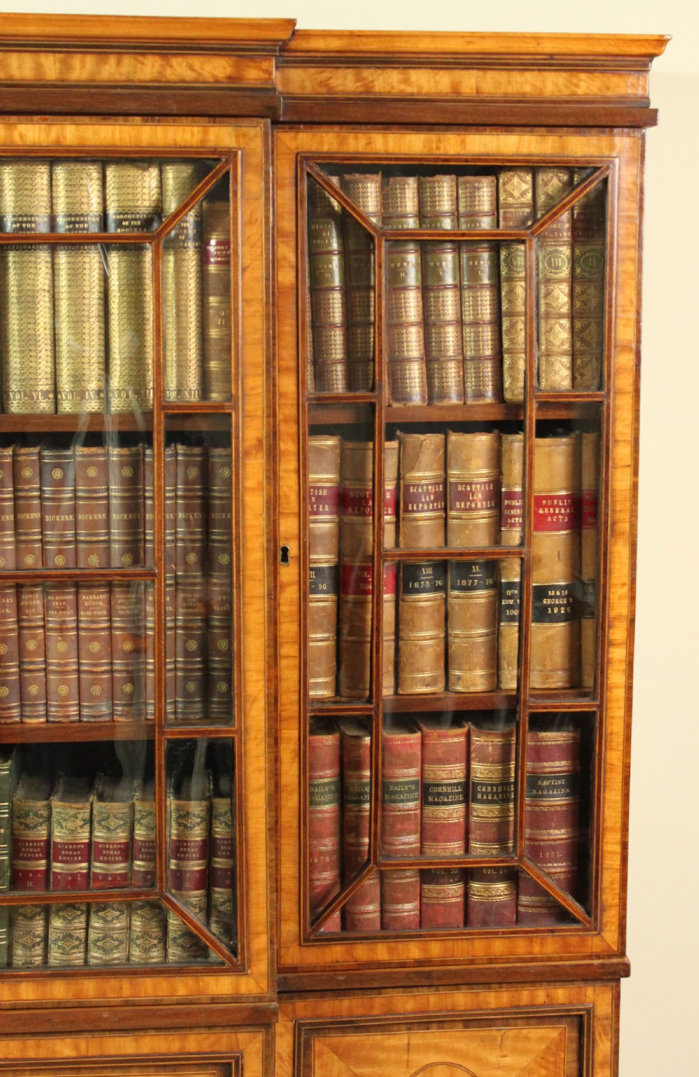 A four-door Georgian breakfront bookcase crafted from golden satinwood featuring geometric astragal glazing bars above four oval inlaid cupboard doors. View IV
