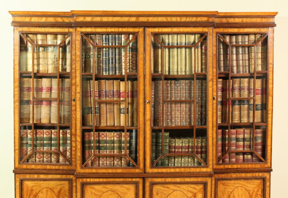 A four-door Georgian breakfront bookcase crafted from golden satinwood featuring geometric astragal glazing bars above four oval inlaid cupboard doors. View V