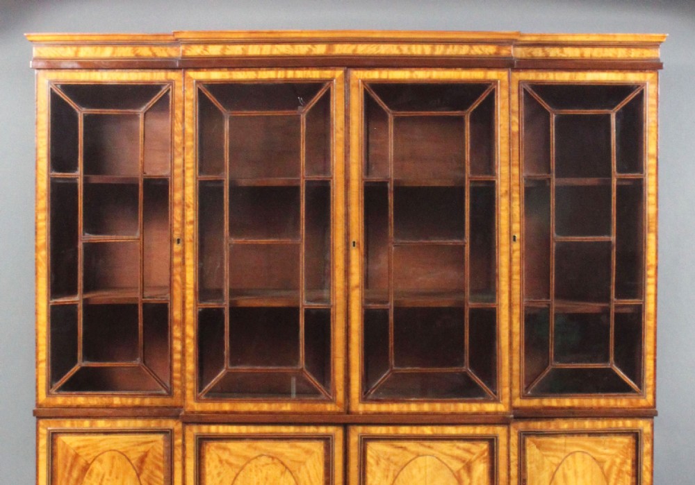 A four-door Georgian breakfront bookcase crafted from golden satinwood featuring geometric astragal glazing bars above four oval inlaid cupboard doors. View VI