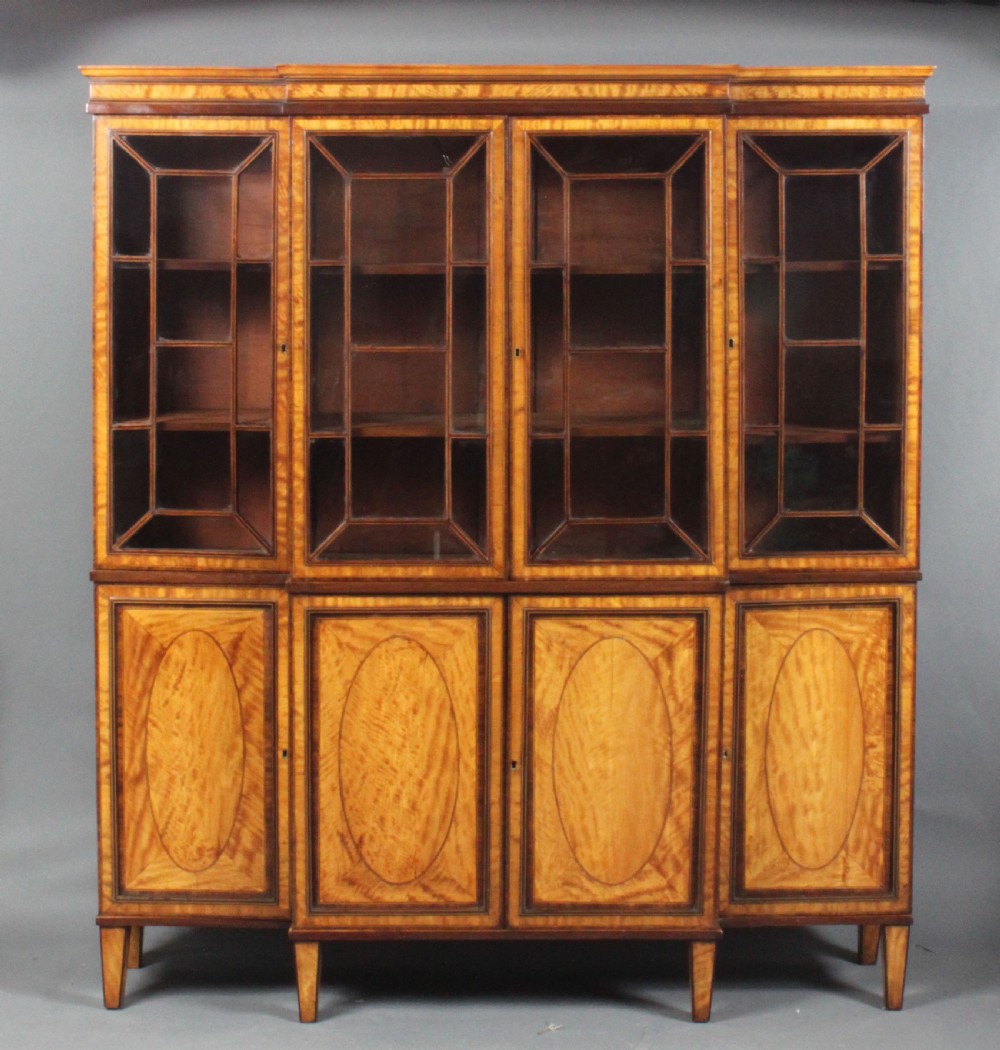A four-door Georgian breakfront bookcase crafted from golden satinwood featuring geometric astragal glazing bars above four oval inlaid cupboard doors. View VIII