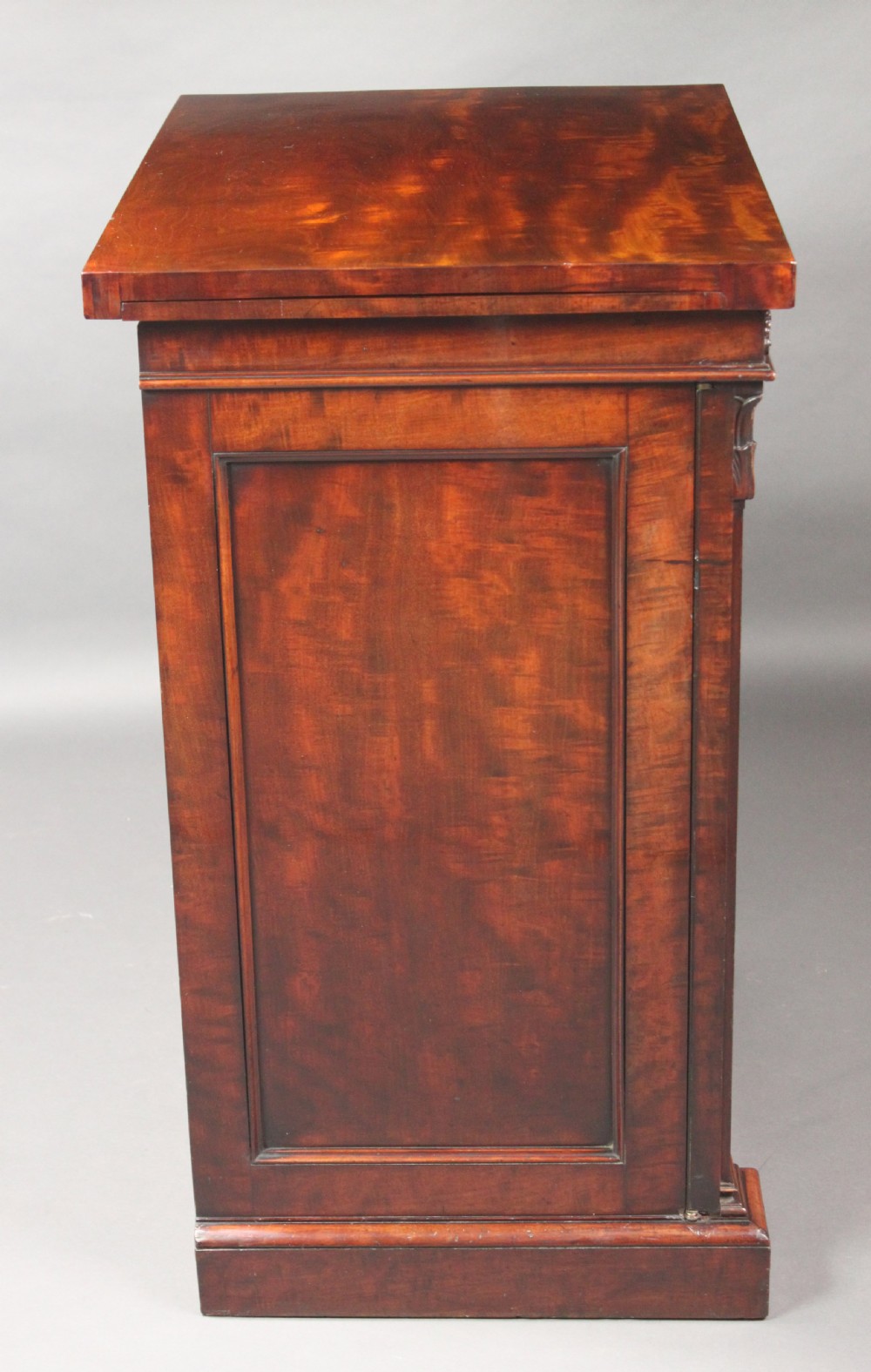 A nineteenth-century flame mahogany library cabinet featuring carved pilasters, reeded side columns, and a single recessed panel door set on a solid plinth base. View II
