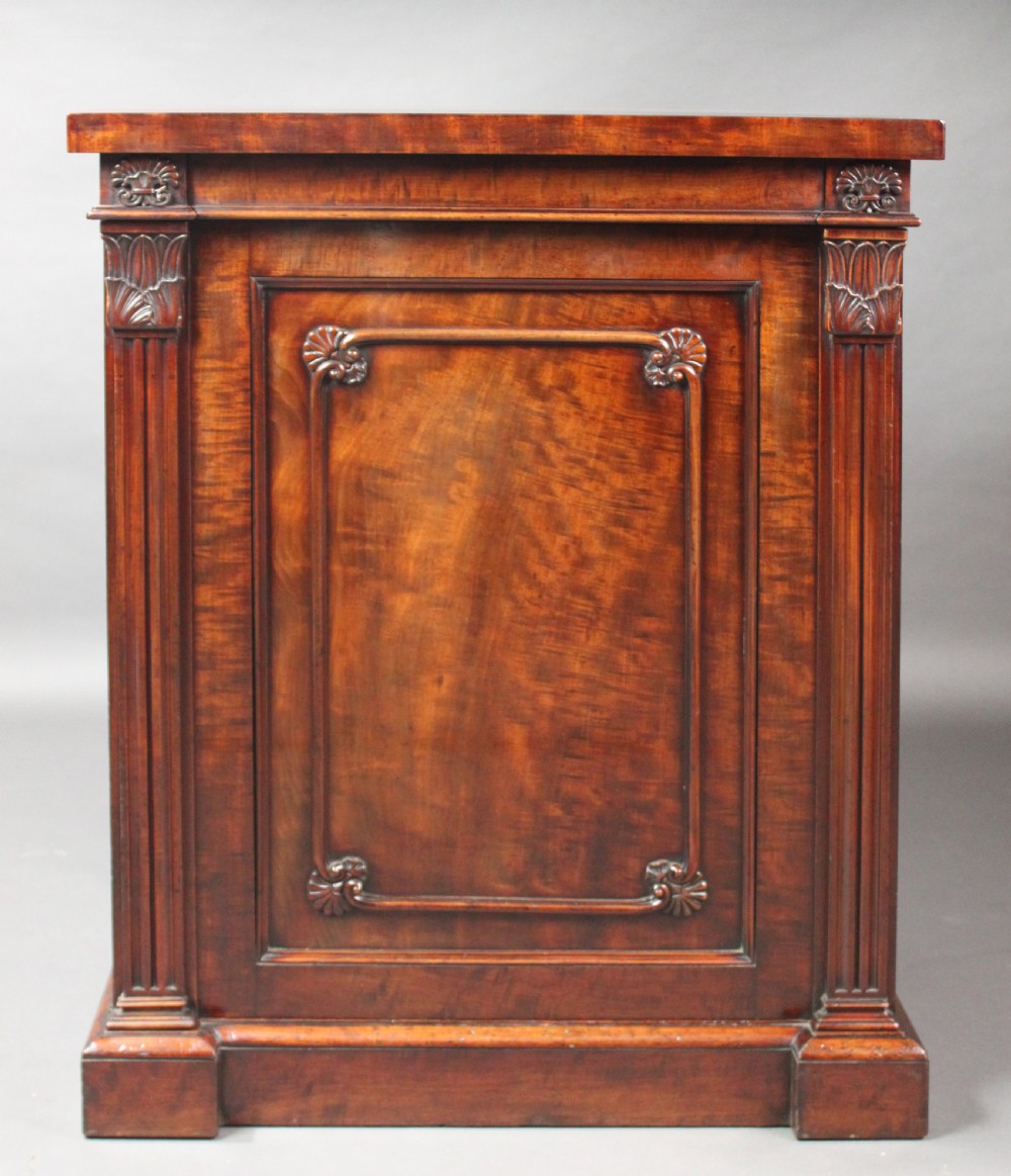 A nineteenth-century flame mahogany library cabinet featuring carved pilasters, reeded side columns, and a single recessed panel door set on a solid plinth base. View VI