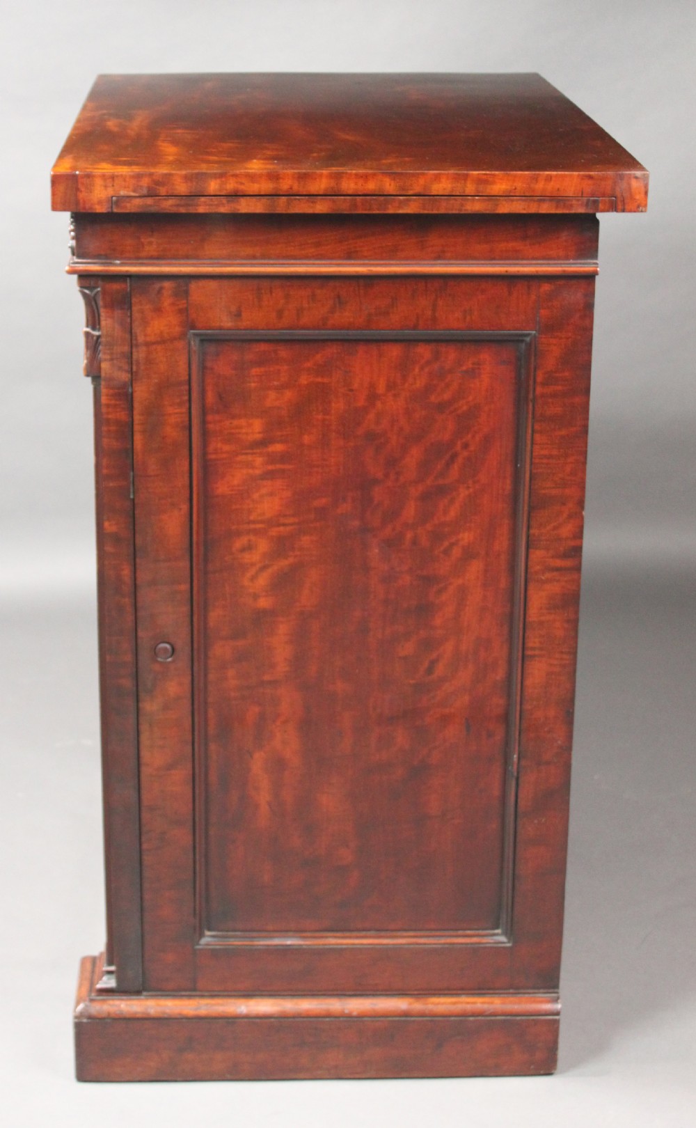 A nineteenth-century flame mahogany library cabinet featuring carved pilasters, reeded side columns, and a single recessed panel door set on a solid plinth base. View VIII