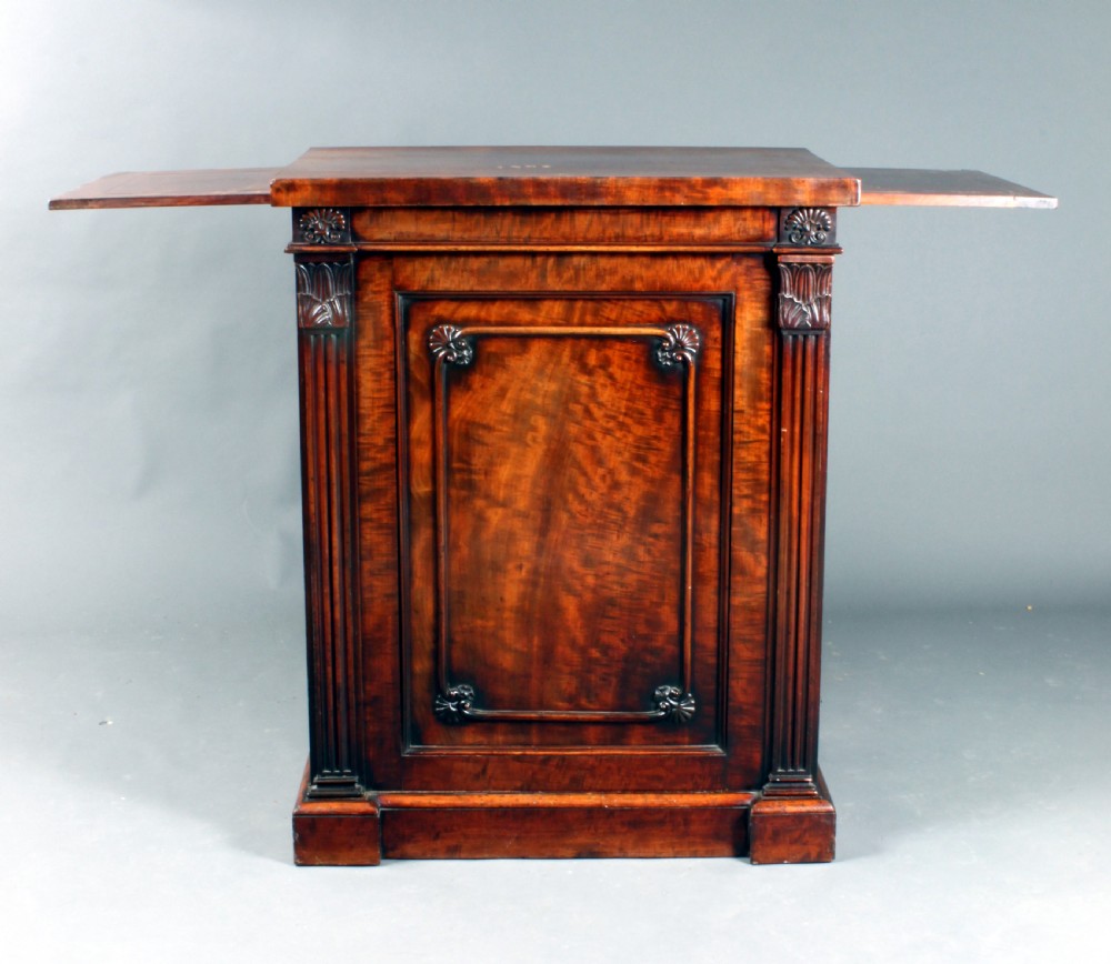 A nineteenth-century flame mahogany library cabinet featuring carved pilasters, reeded side columns, and a single recessed panel door set on a solid plinth base. View XI