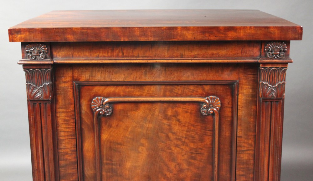 A nineteenth-century flame mahogany library cabinet featuring carved pilasters, reeded side columns, and a single recessed panel door set on a solid plinth base. View XII