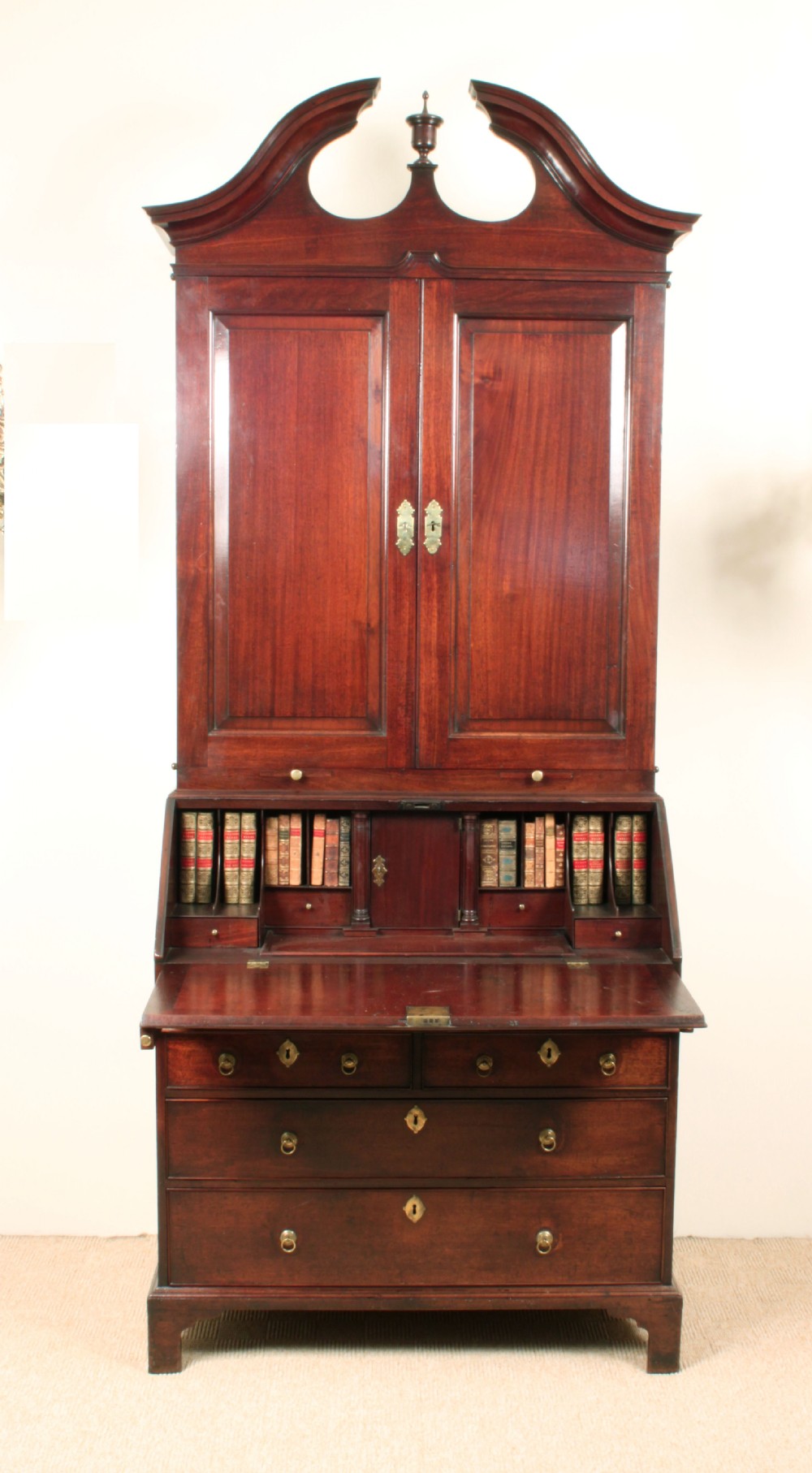 A Georgian mahogany bureau bookcase featuring a swan-neck pediment top, twin panelled upper doors, a slant-front writing bureau with fitted pigeonholes, and three base drawers on bracket feet.