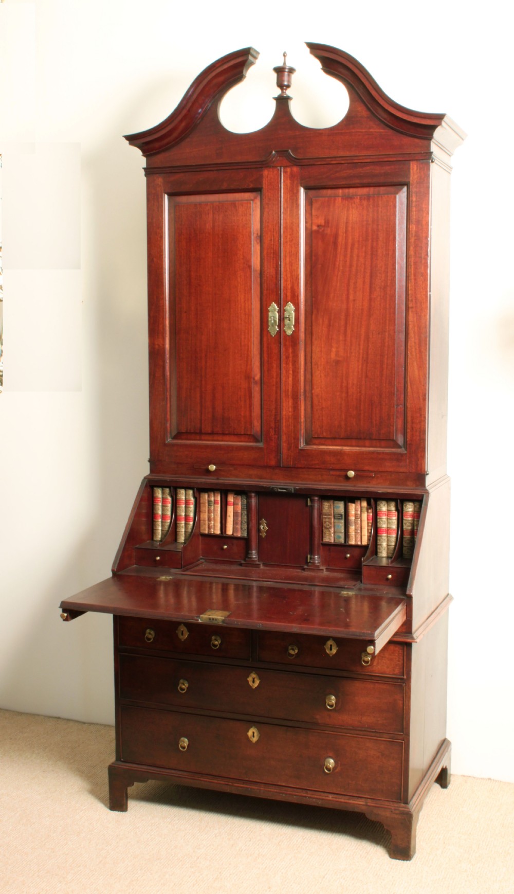 A Georgian mahogany bureau bookcase featuring a swan-neck pediment top, twin panelled upper doors, a slant-front writing bureau with fitted pigeonholes, and three base drawers on bracket feet. View IX