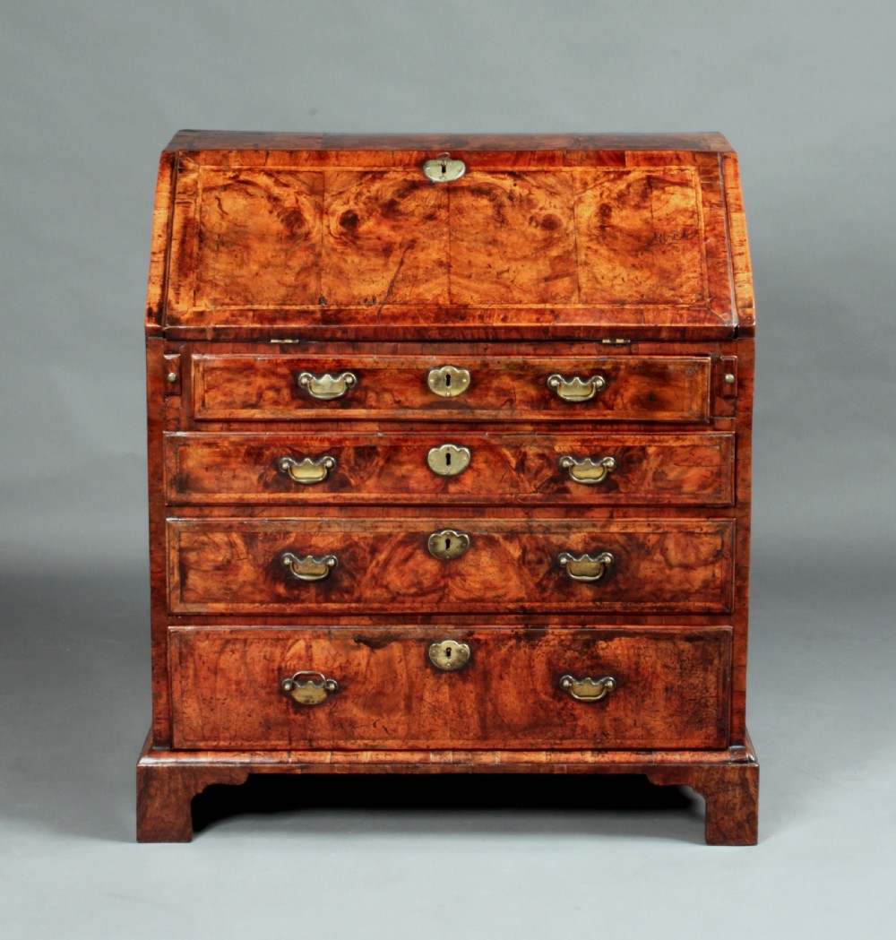 An early 18th-century George I walnut bureau featuring a sloping fall-front lid above four graduated drawers with brass drop handles and bracket feet.
