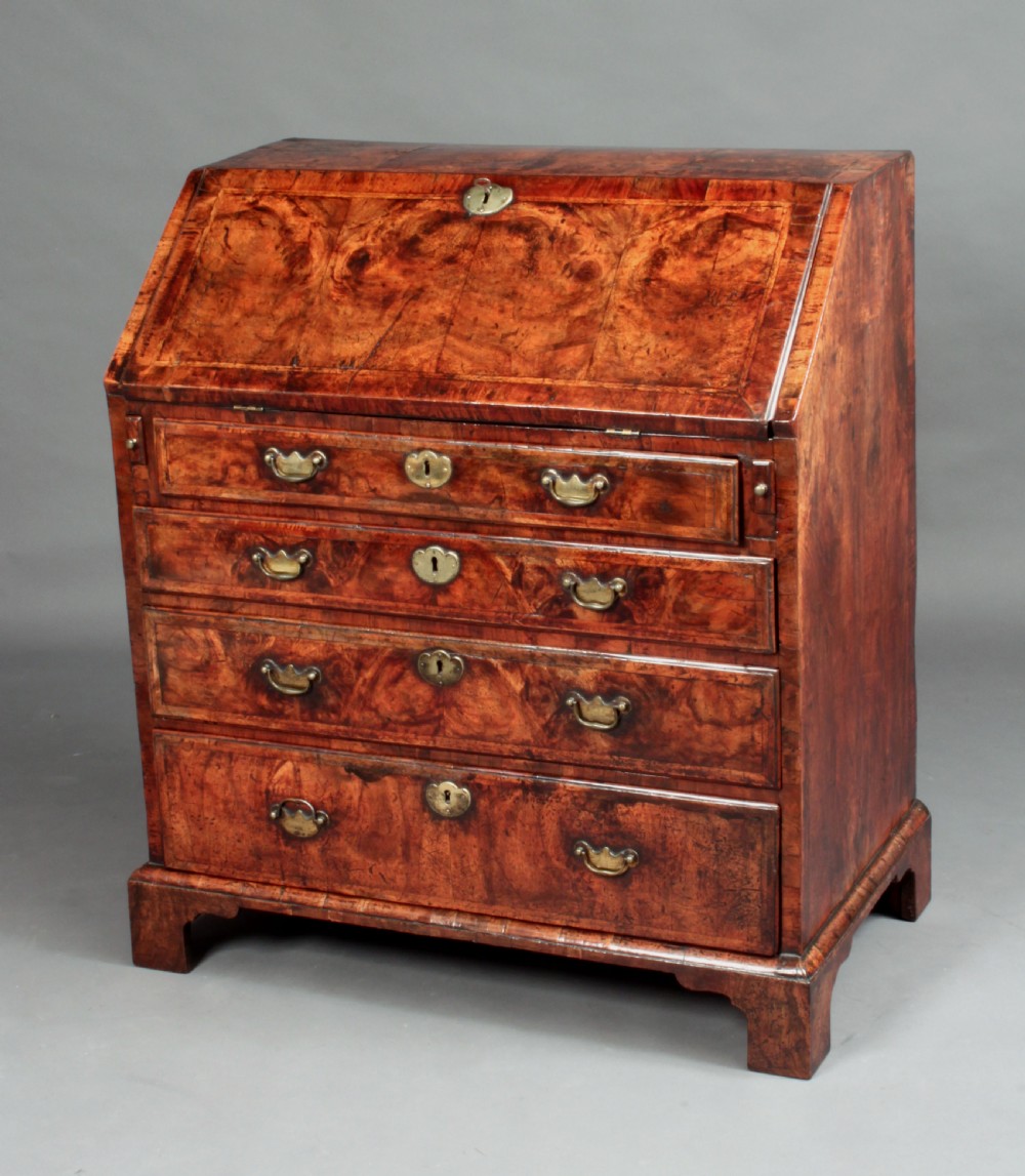 An early 18th-century George I walnut bureau featuring a sloping fall-front lid above four graduated drawers with brass drop handles and bracket feet. View II