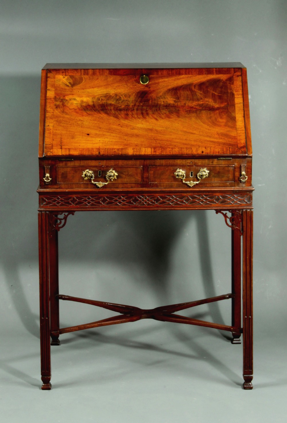 An antique Chippendale style dark mahogany slant-front bureau mounted on a tall stand with straight carved legs and an X-frame stretcher. View II