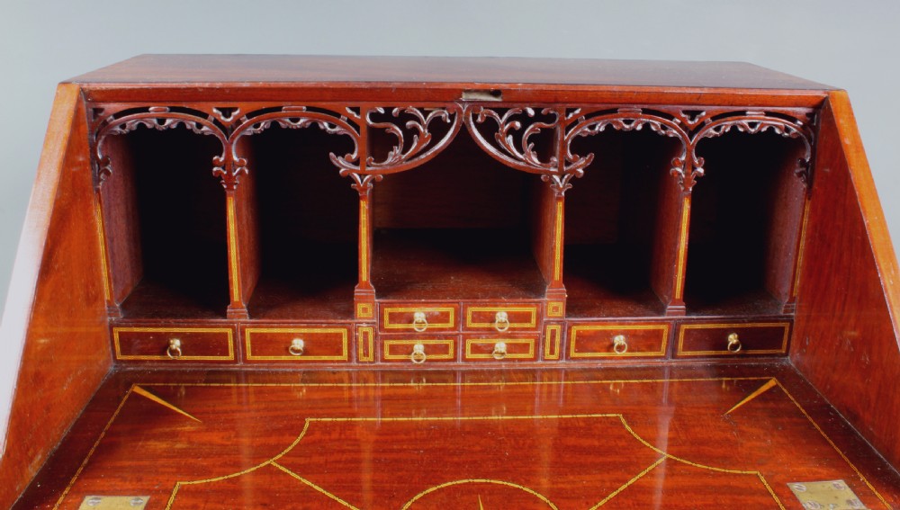 An antique Chippendale style dark mahogany slant-front bureau mounted on a tall stand with straight carved legs and an X-frame stretcher. View III