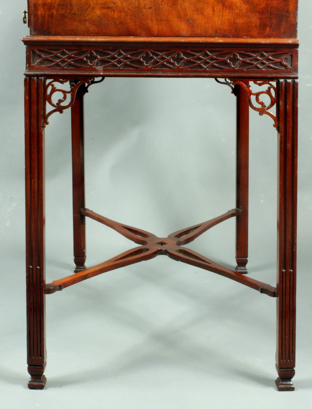 An antique Chippendale style dark mahogany slant-front bureau mounted on a tall stand with straight carved legs and an X-frame stretcher. View V