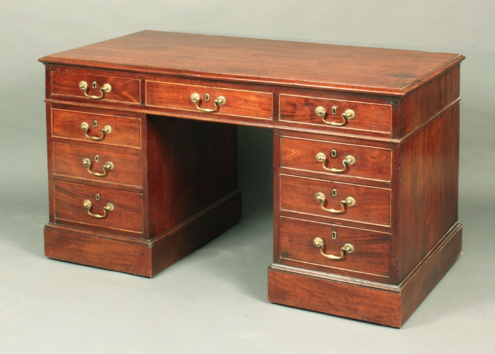 An antique Chippendale mahogany pedestal desk featuring nine cockbeaded drawers with brass swan-neck handles around a central kneehole, resting on twin plinth bases.