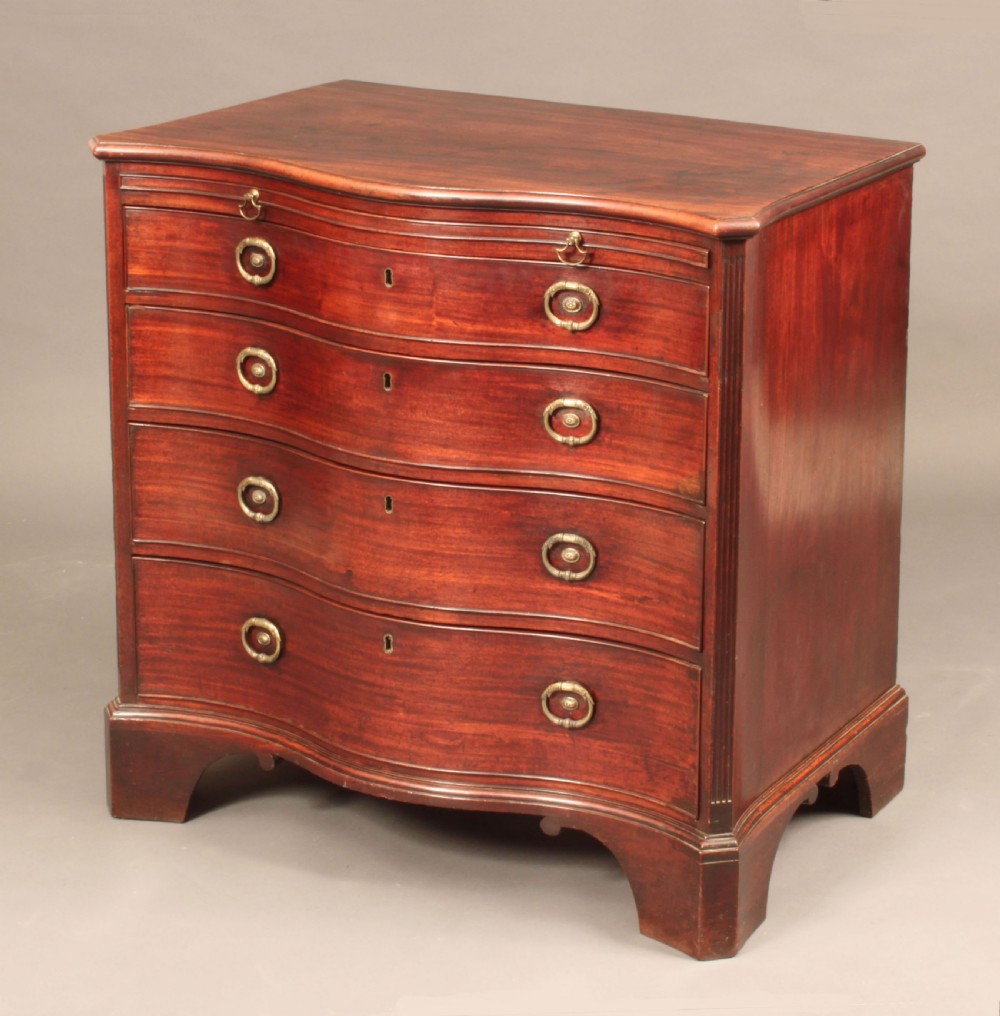 An antique George III mahogany chest of drawers featuring a curved serpentine front, four graduated drawers with brass handles, and sturdy bracket feet.