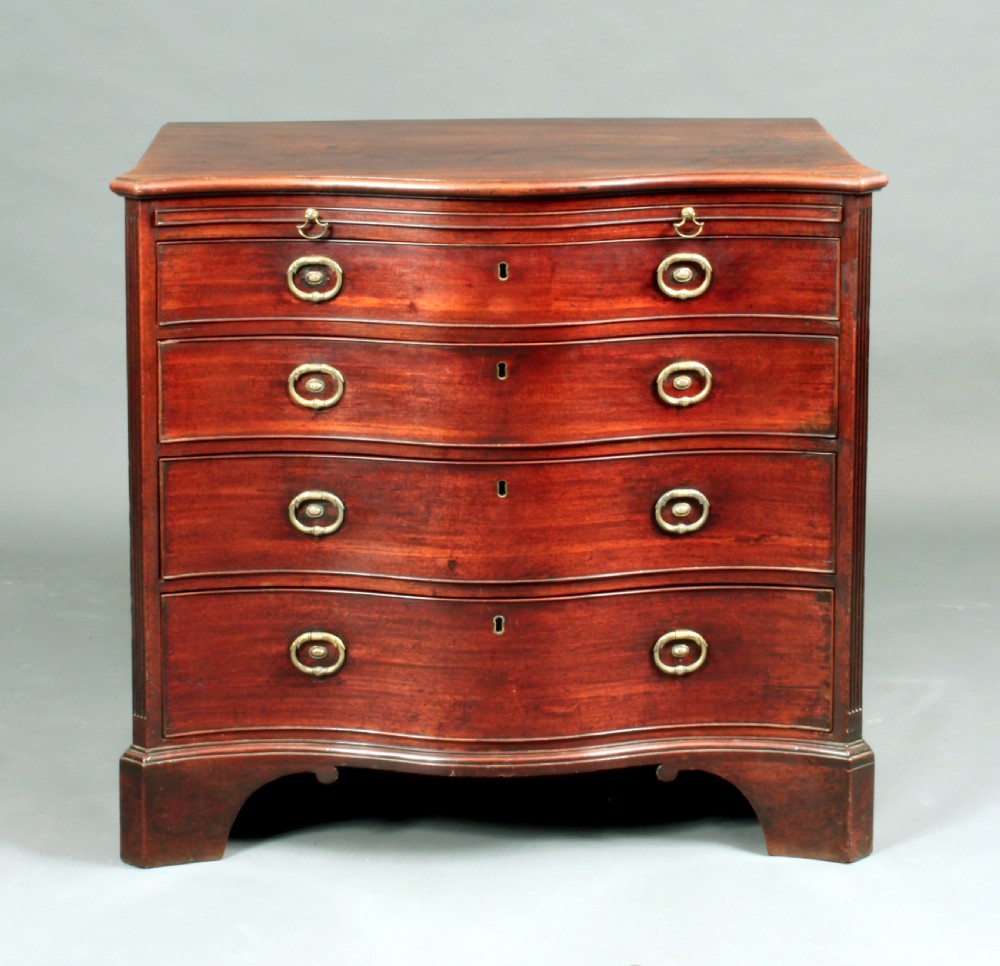 An antique George III mahogany chest of drawers featuring a curved serpentine front, four graduated drawers with brass handles, and sturdy bracket feet. View II