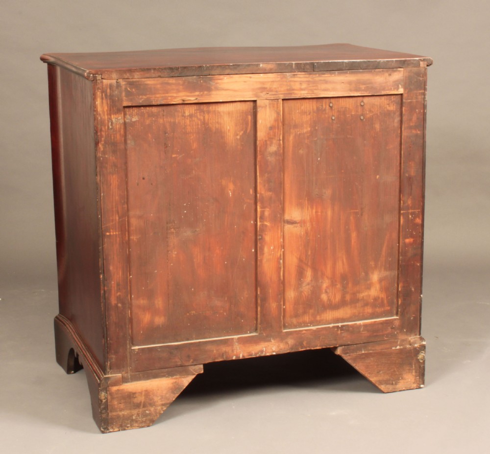 An antique George III mahogany chest of drawers featuring a curved serpentine front, four graduated drawers with brass handles, and sturdy bracket feet. View V