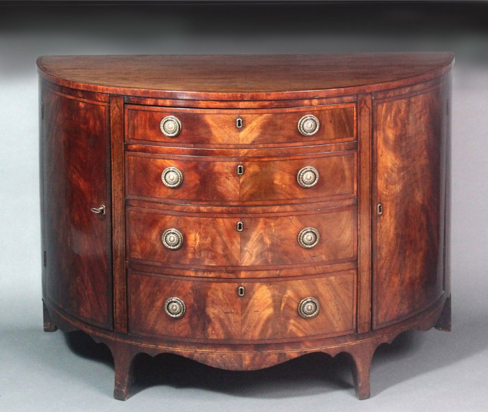 A late 18th-century George III flame mahogany demi-lune commode featuring four central drawers flanked by side cupboards, resting on bracket feet.