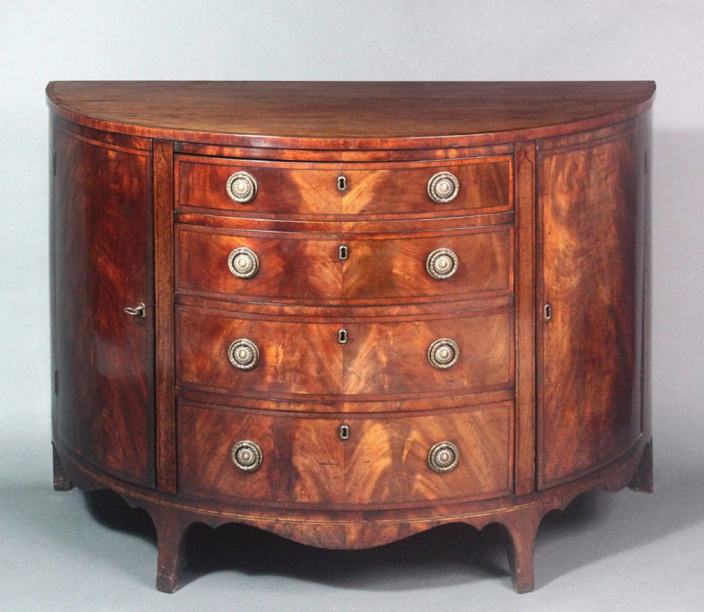A late 18th-century George III flame mahogany demi-lune commode featuring four central drawers flanked by side cupboards, resting on bracket feet. View III