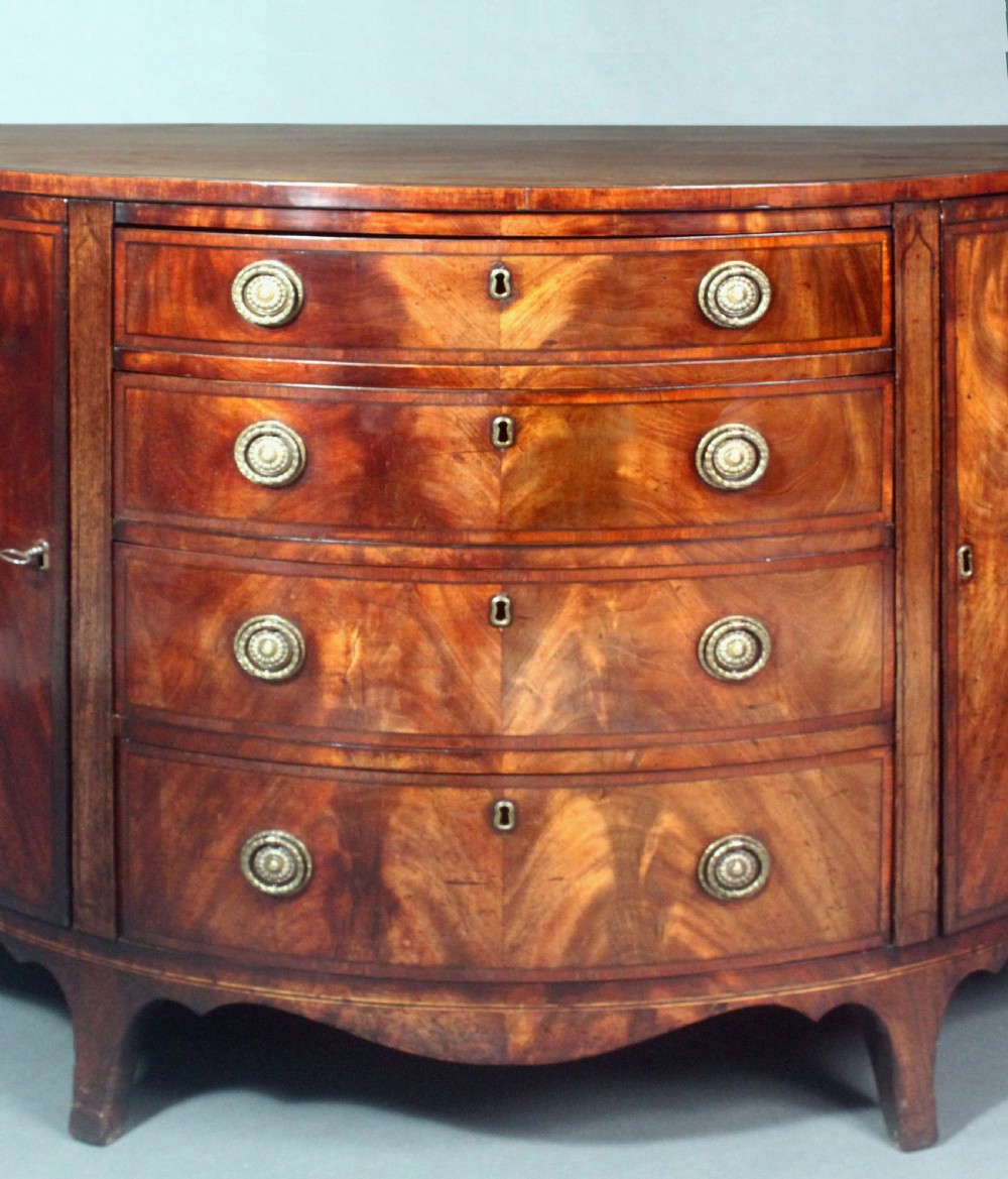 A late 18th-century George III flame mahogany demi-lune commode featuring four central drawers flanked by side cupboards, resting on bracket feet. View VI