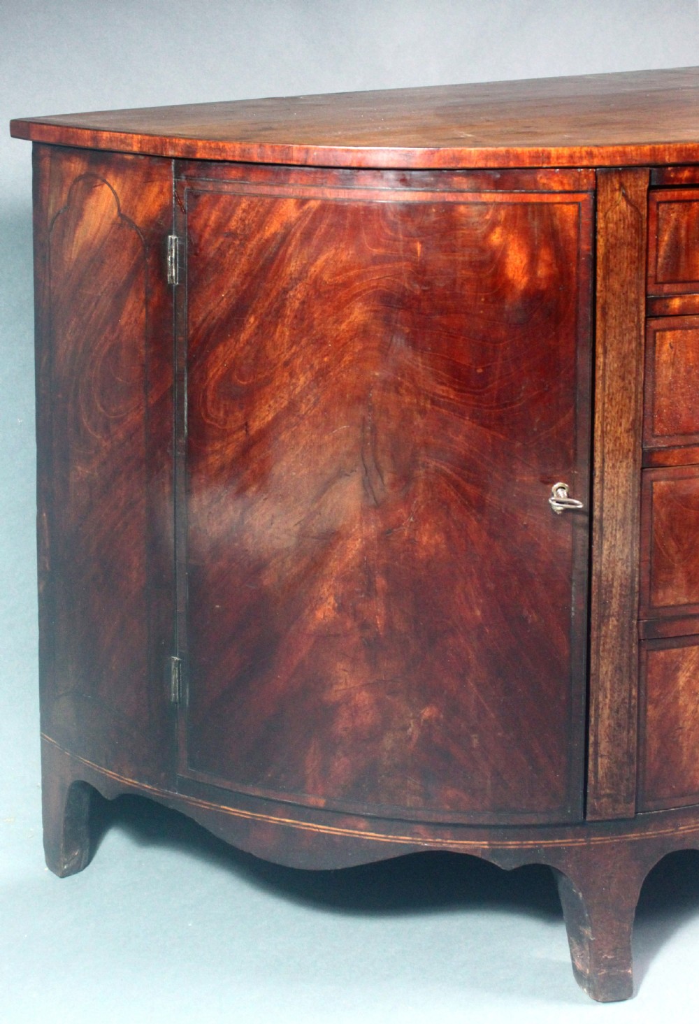 A late 18th-century George III flame mahogany demi-lune commode featuring four central drawers flanked by side cupboards, resting on bracket feet. View VII