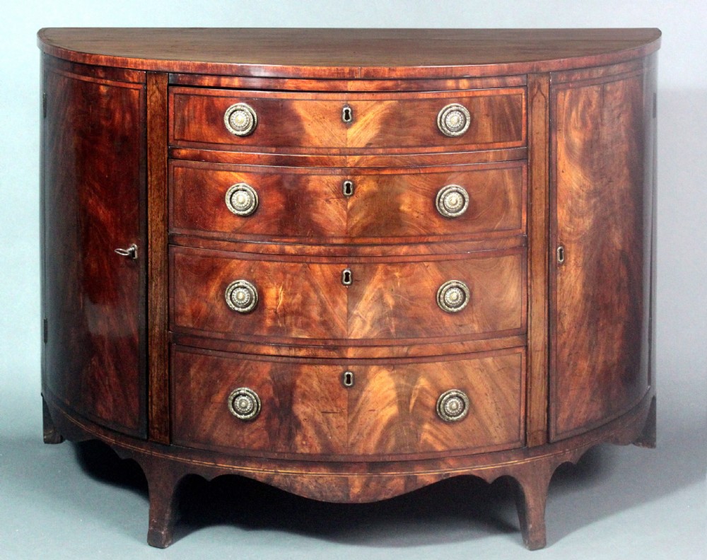 A late 18th-century George III flame mahogany demi-lune commode featuring four central drawers flanked by side cupboards, resting on bracket feet. View VIII