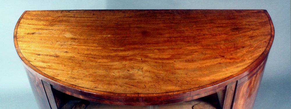 A late 18th-century George III flame mahogany demi-lune commode featuring four central drawers flanked by side cupboards, resting on bracket feet. View XI