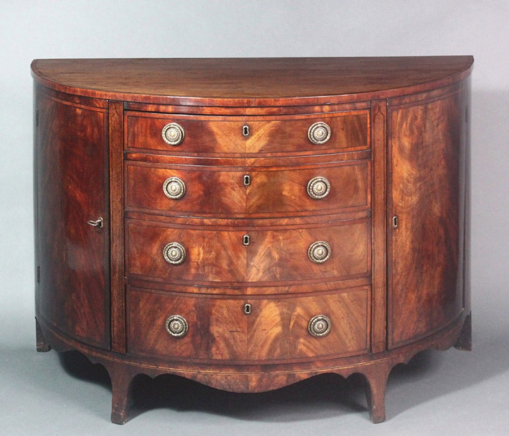 A late 18th-century George III flame mahogany demi-lune commode featuring four central drawers flanked by side cupboards, resting on bracket feet. View XIV