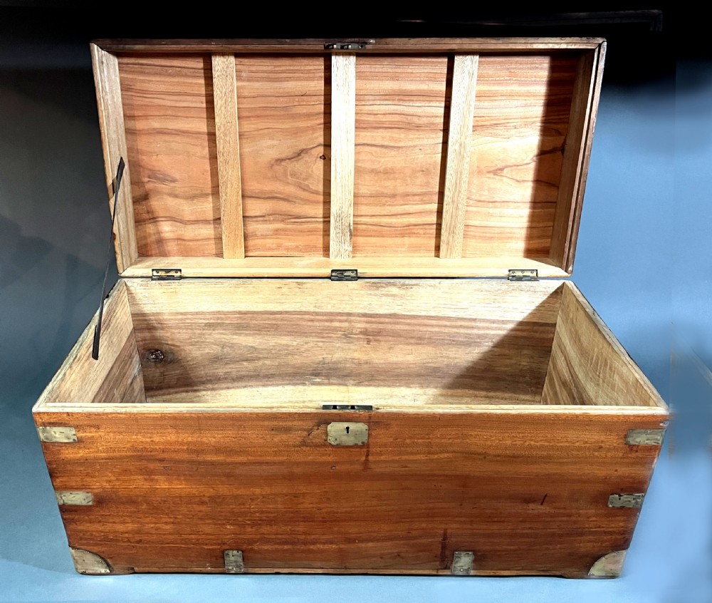 An antique rectangular camphor wood campaign chest featuring recessed brass handles, corner brackets, and a central brass escutcheon. View V