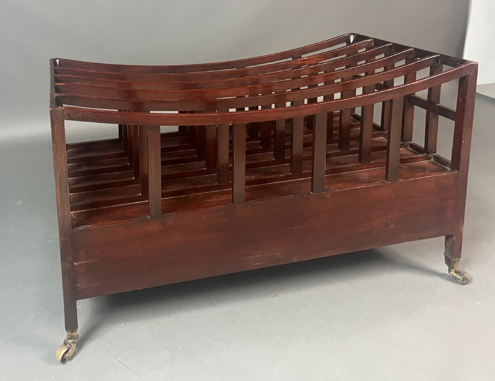 An antique Georgian mahogany Canterbury featuring a slatted concave top section, four internal compartments, two lower drawers with brass knobs, and slim tapered legs on brass castors. View II