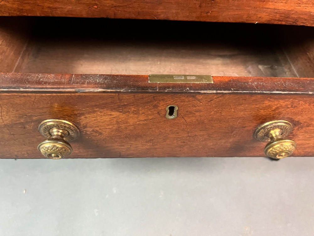 An antique Georgian mahogany Canterbury featuring a slatted concave top section, four internal compartments, two lower drawers with brass knobs, and slim tapered legs on brass castors. View VI
