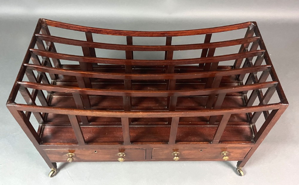 An antique Georgian mahogany Canterbury featuring a slatted concave top section, four internal compartments, two lower drawers with brass knobs, and slim tapered legs on brass castors. View VIII