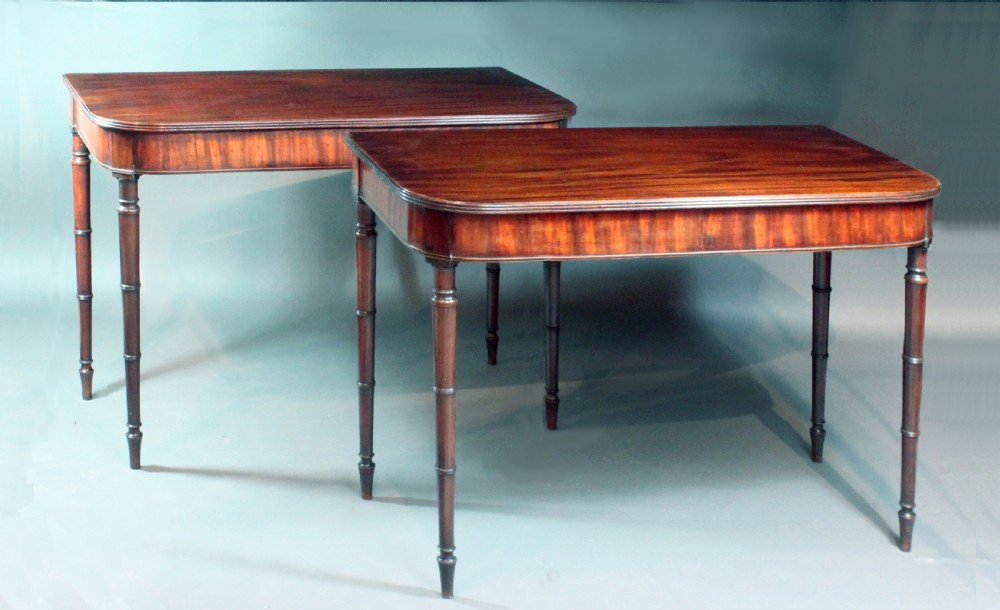 A matching pair of Georgian mahogany serving tables featuring flame veneer aprons and turned tapered legs.