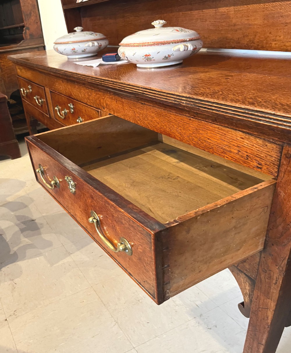 An antique oak dresser featuring a three-drawer base with brass swan-neck handles, topped with a tall open three-shelf plate rack. View IV