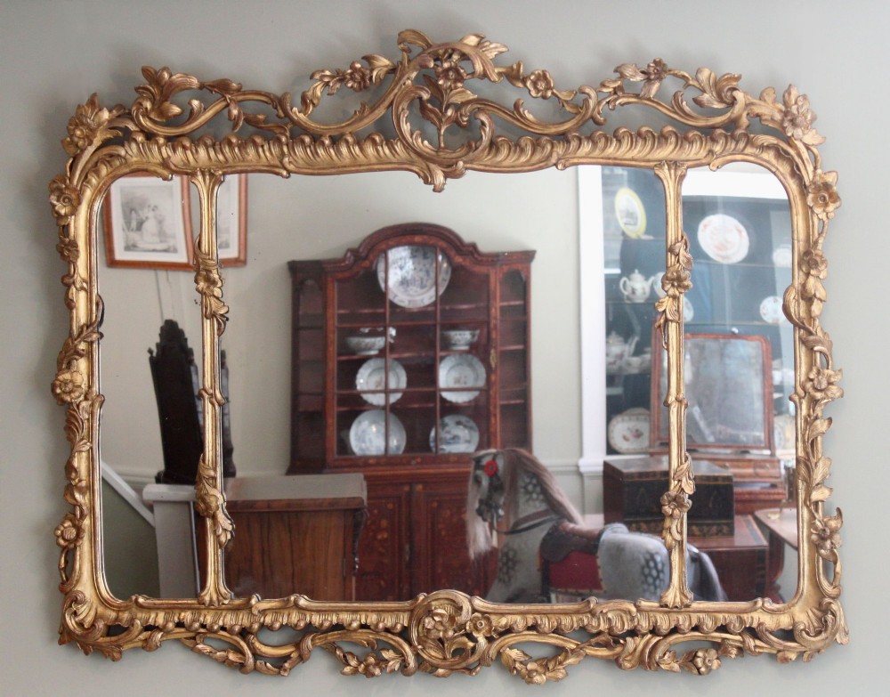 An ornate horizontal Chippendale giltwood overmantel mirror featuring intricate floral and leaf carvings around three glass panels.