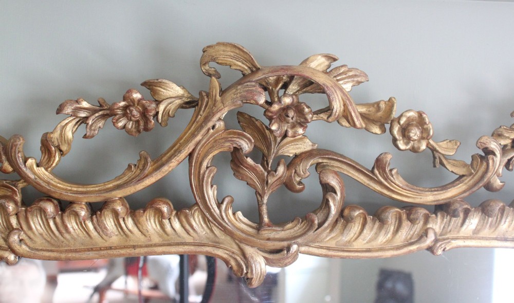 An ornate horizontal Chippendale giltwood overmantel mirror featuring intricate floral and leaf carvings around three glass panels. View V