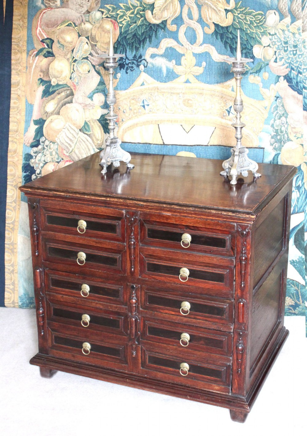 Dark brown Charles II oak chest of drawers featuring geometric moulded drawer fronts and brass drop handles.
