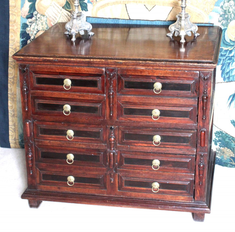 Dark brown Charles II oak chest of drawers featuring geometric moulded drawer fronts and brass drop handles. View II