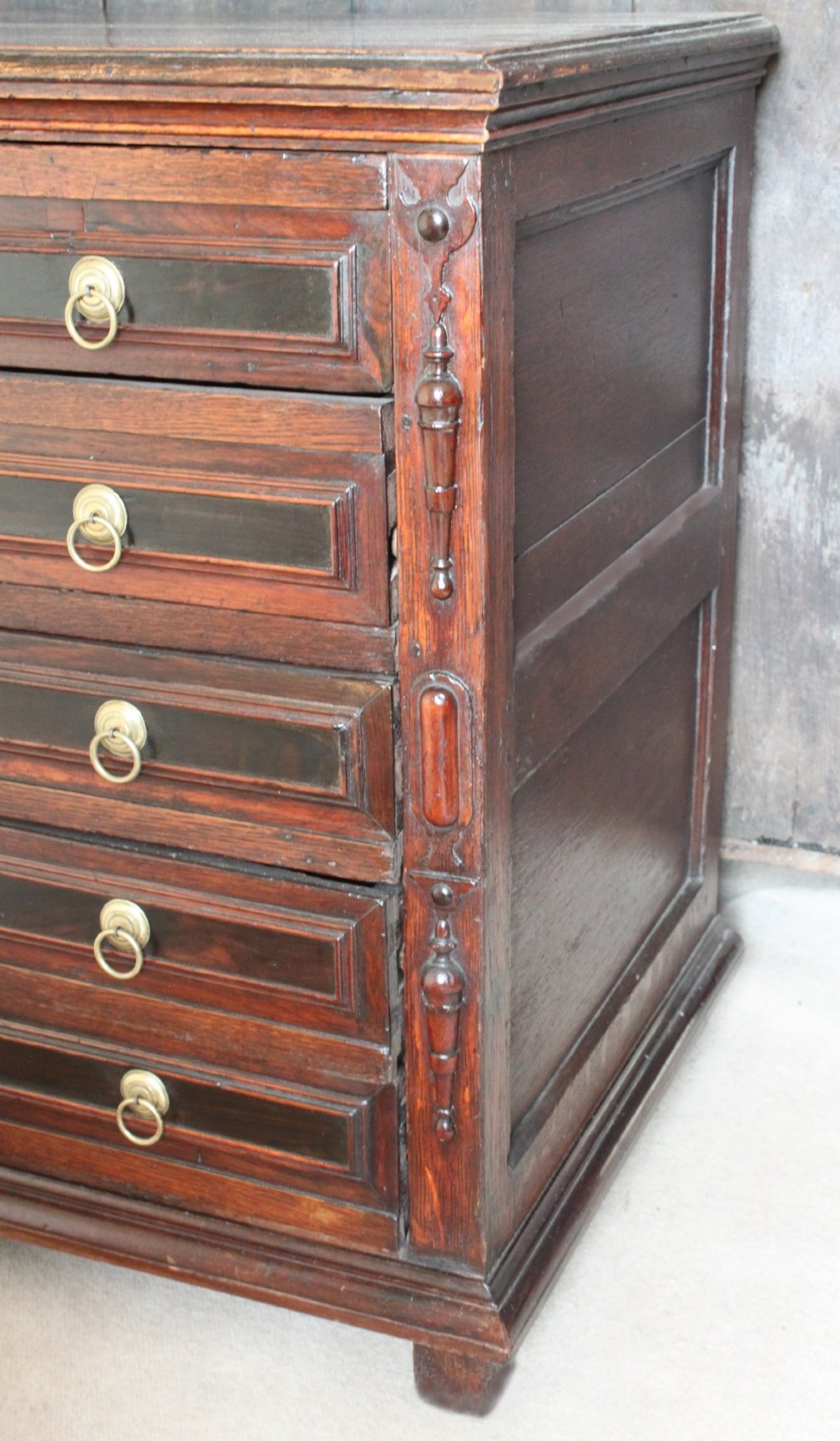 Dark brown Charles II oak chest of drawers featuring geometric moulded drawer fronts and brass drop handles. View V