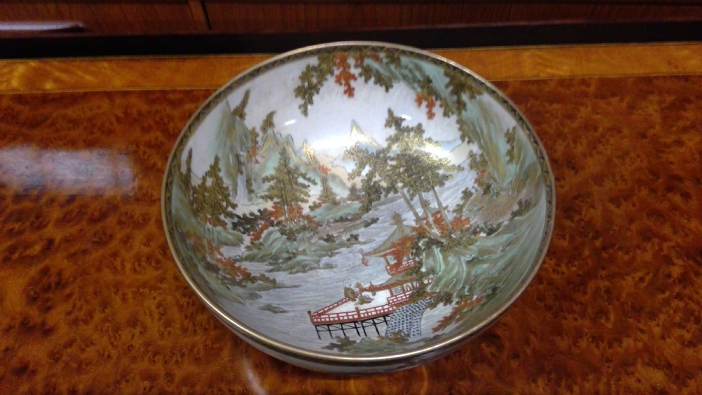 A circular Japanese Satsuma ceramic bowl featuring a hand-painted interior landscape with pagodas, trees, mountains, and gilt accents.