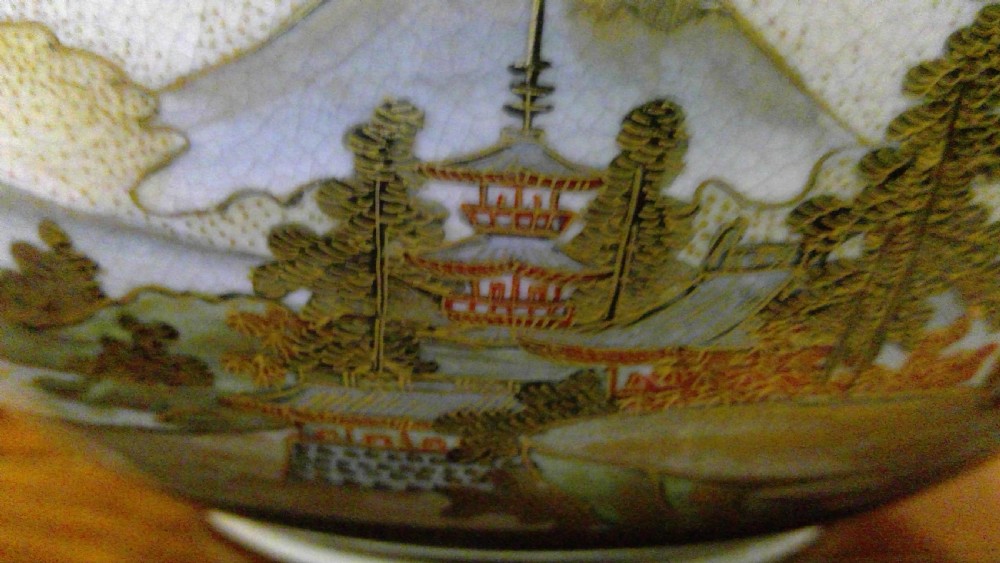 A circular Japanese Satsuma ceramic bowl featuring a hand-painted interior landscape with pagodas, trees, mountains, and gilt accents. View X