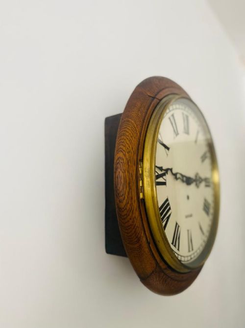 fig 1. A circular vintage Garrard wall clock featuring a warm oak frame, a brass bezel, and a cream dial with black Roman numerals.