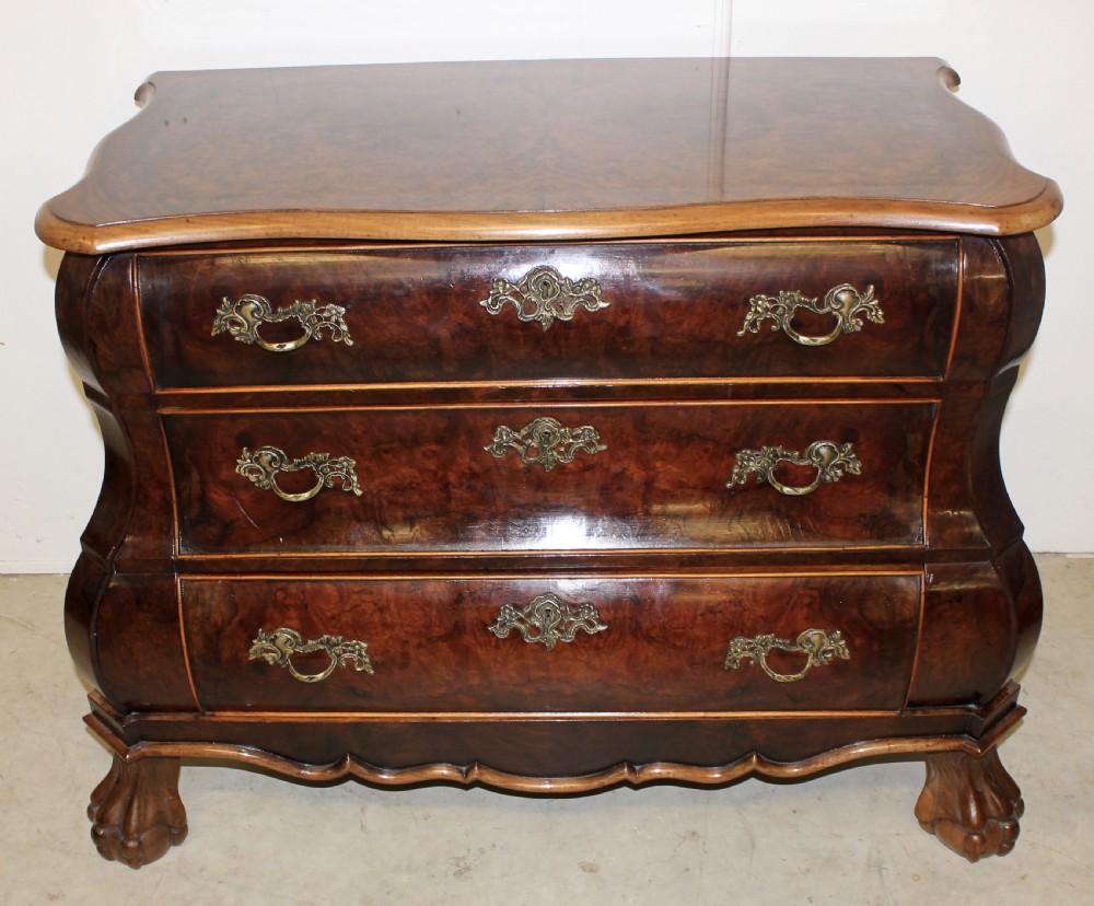 A Dutch burr walnut bombe chest of drawers featuring three shaped drawers, ornate cast brass handles, and claw and ball feet.
