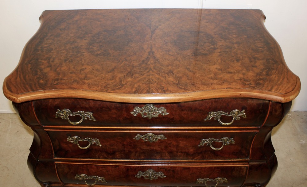 A Dutch burr walnut bombe chest of drawers featuring three shaped drawers, ornate cast brass handles, and claw and ball feet. View II