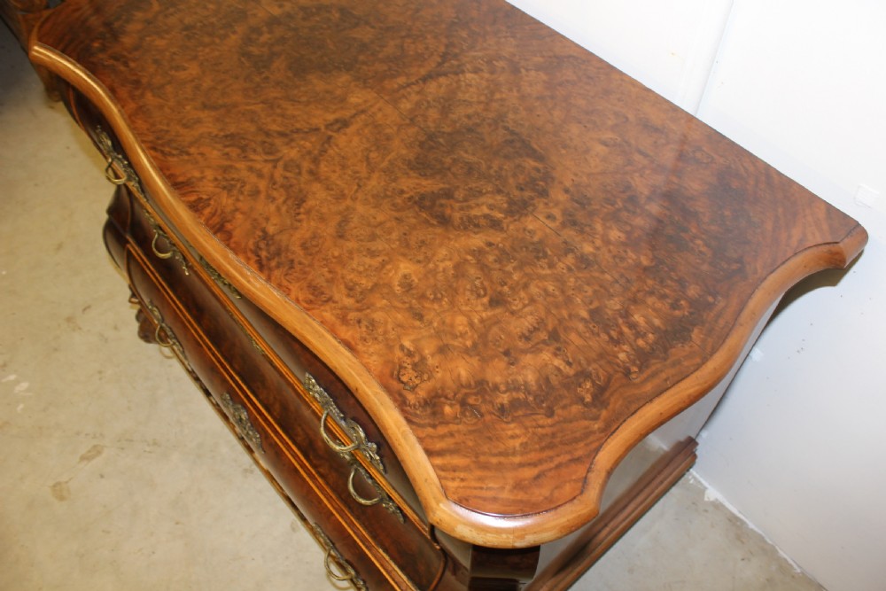 A Dutch burr walnut bombe chest of drawers featuring three shaped drawers, ornate cast brass handles, and claw and ball feet. View III