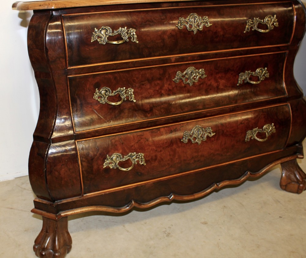 A Dutch burr walnut bombe chest of drawers featuring three shaped drawers, ornate cast brass handles, and claw and ball feet. View IV